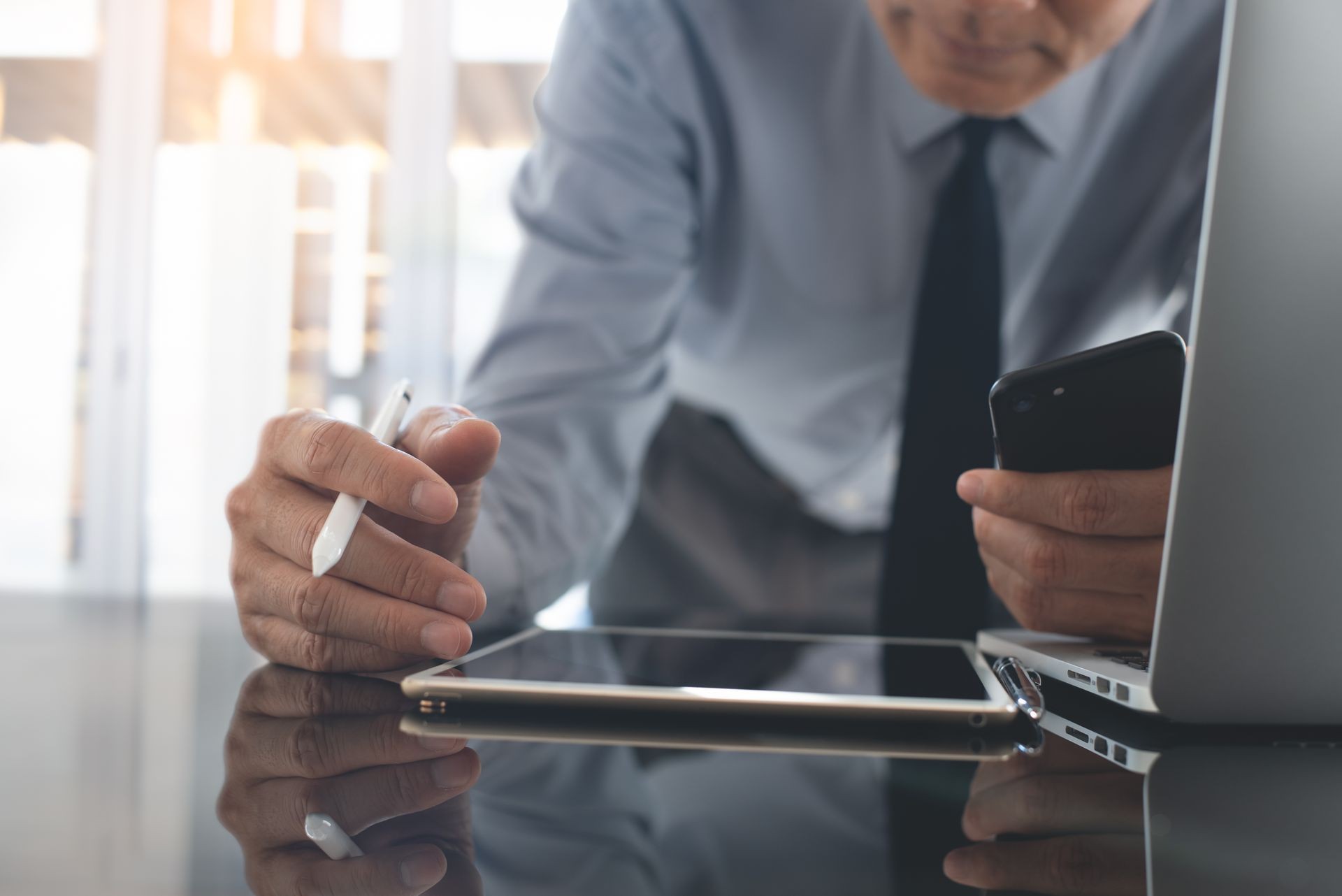 Business finance and technology concept. Multitasking asian businessman, accountant using digital tablet with stylus pen and mobile smart phone while working on laptop computer in modern office